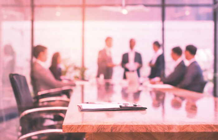 Business team sitting around boardroom table, tinted in a rose-coloured hue